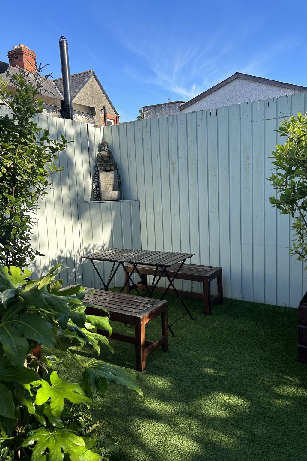 A small paved back garden with bench seating, plants and a decorative statue
