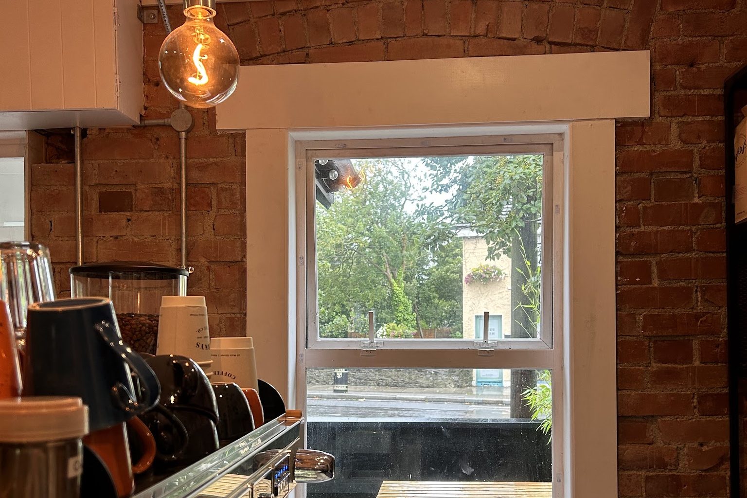 An exposed-brick espresso bar with a hanging pendant light and a window onto Raheny's Main Street